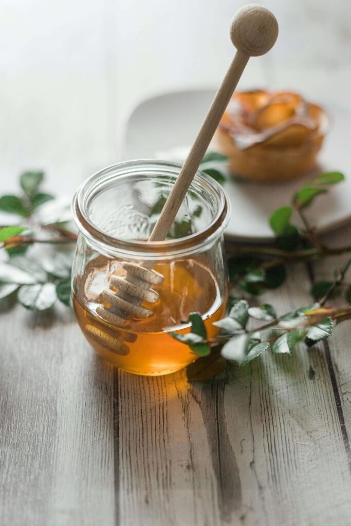 Clear glass jar filled with golden honey on a wooden table, illustrating the natural purity and smooth texture of the product.